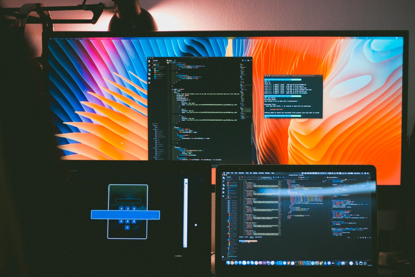 Developer's screens showing colorful code and abstract waves at night.